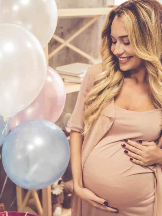 Beautiful pregnant woman is smoothing her tummy and smiling during baby shower