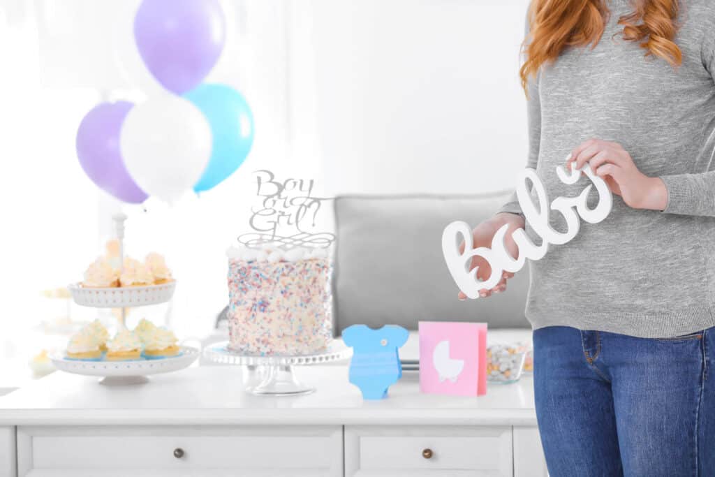 woman holding a baby sign with gender reveal items in the background